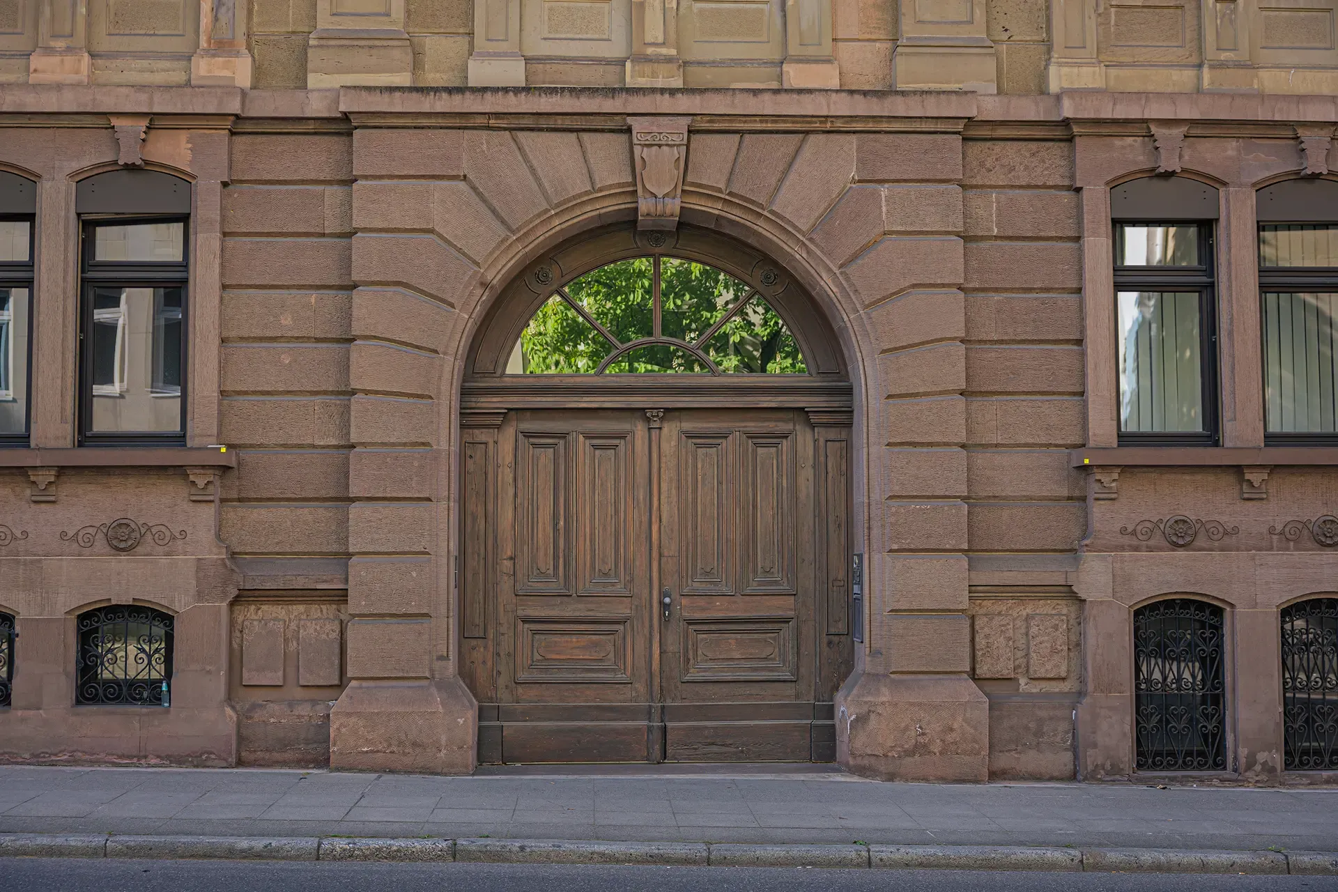 Historisches Hauseingangsportal mit zweiflügeliger Holztür in einer Sandsteinfassade.