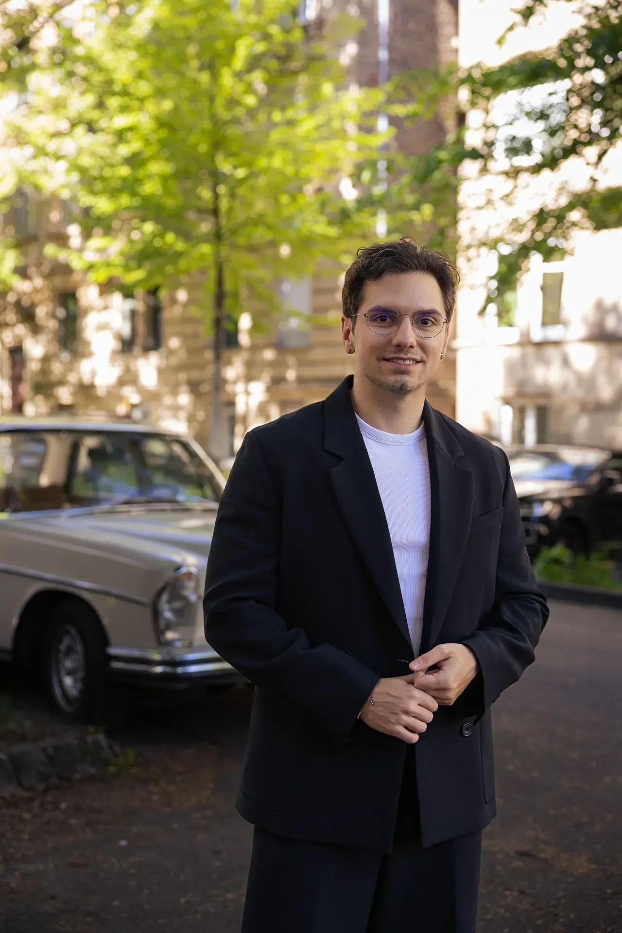 Porträt von Przemyslaw Wrobel im dunklen Sakko, im Hintergrund ein Oldtimer und begrünte Altbauten.